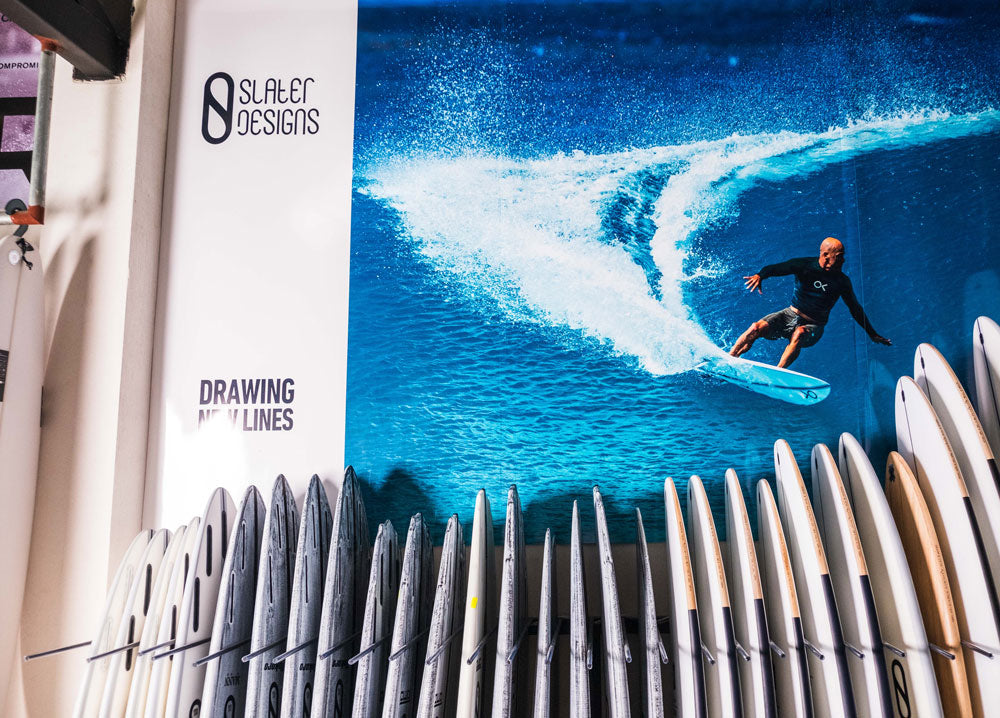 Surfer riding a wave with 'Slater Designs' branding on a wall.
